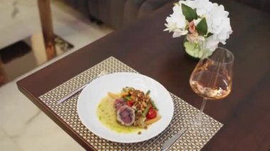 Modern bir restoranda bir kadın akşam yemeği için bir bardak pembe şarap ve lezzetli bir tabak yemek ısmarlar.