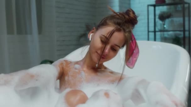 Πορτρέτο closeup στην κάμερα χαριτωμένο κυρία λάβει ένα μπάνιο με διαφήμιση φούσκα αίσθηση χαλαρή ακούει μουσική από ακουστικά — Αρχείο Βίντεο