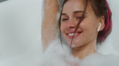 Küvette içi köpükle dolu seksi bir bayan kulaklıklardan müzik dinlemekten zevk alıyor. ARRI Alexa Mini 'de çekilen.