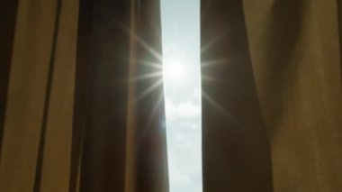 Güneş büyük bir pencerenin krema perdelerinden parlıyor.