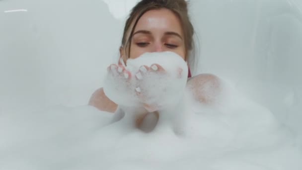 Glückliche und aufgeregte Dame nimmt ein Bad mit voller Blase pustet sie die Blase und hört Musik aus den drahtlosen Kopfhörern — Stockvideo
