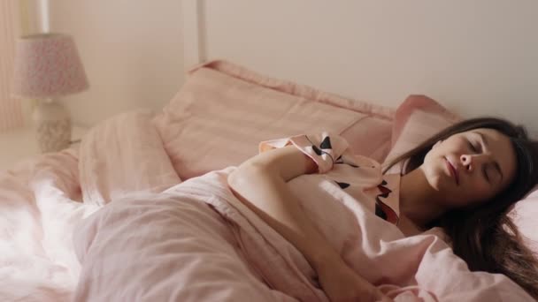 En mycket snygg kvinna i rosa pyjamas vaknade upp ur sömnen, leende som hon är mycket glad att börja dagen — Stockvideo