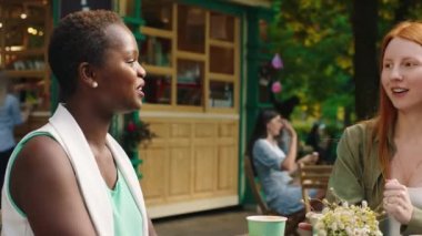 Çok güzel bir Afrikalı kadın ve arkadaşları sarı saçlı ve kızıl saçlı kadın kafede eğleniyorlar. Büyük bir gülümsemeyle dostça sohbet ediyorlar.