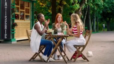 Parkın ortasında güzel, çok ırklı genç kadınlar pastanede birlikte vakit geçiriyorlar. Biraz tatlı yiyorlar ve kendilerini harika hissediyorlar.