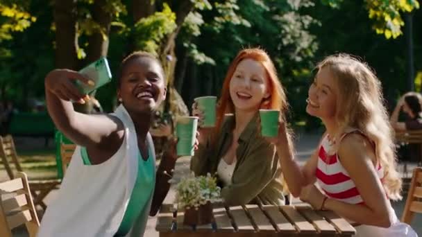 African beautiful lady with a large smile and other two perfect looking ladies taking selfies at cafe while drinking some coffee in the middle of park — Stock Video