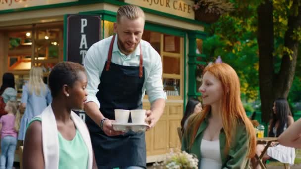 En medio del parque en la terraza del café grupo de señoras multiétnicas disfrutar del tiempo juntos barista trae las señoras de café fresco toma el café y empezar a conversar que están sonriendo y sintiendo — Vídeos de Stock