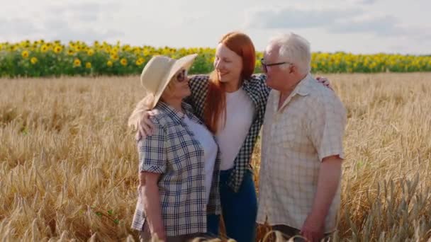 Hermosa sobrina y sus abuelos granjeros abrazándose y posando frente a la cámara en medio del campo de trigo — Vídeos de Stock