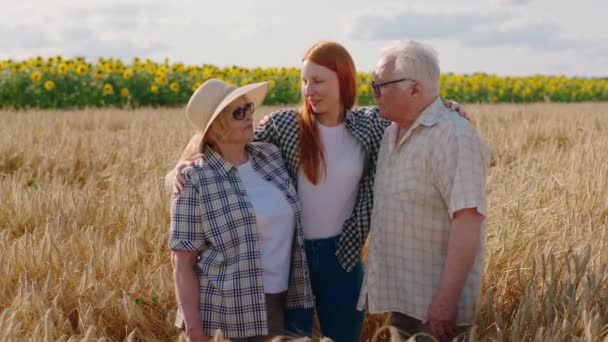 Uprostřed pšeničného pole dobře vypadající staří prarodiče a jejich neteř rádi diskutují o letošní sklizni a objímají se před kamerou — Stock video