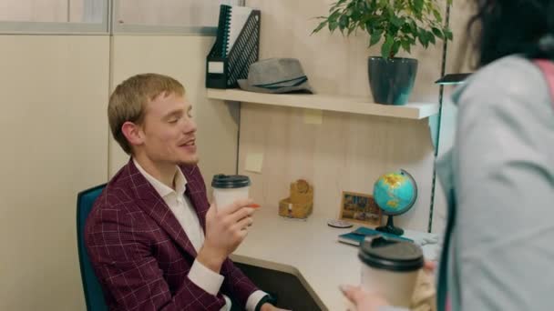 Happy and good looking office manager man at his workplace drink some coffee and have a conversation with his office assistant lady — Stock Video