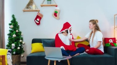 Evde, kanepede güzel görünümlü, gülümseyen, iri bir kadın ve arkadaşı Noel Baba 'nın kırmızı battaniyesiyle birlikte iyi vakit geçiriyorlar.