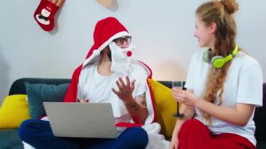 Mutlu gülümseyen koca kadın ve erkek arkadaşı oturma odasında oturmuş Noel Baba battaniyesi giymiş şampanya içiyorlardı.