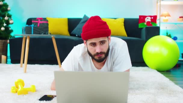 Młody człowiek studiujący w domu online z laptopa bardzo podekscytowany gestykulacją ręką wykonał ciężką pracę leżąc na podłodze — Wideo stockowe