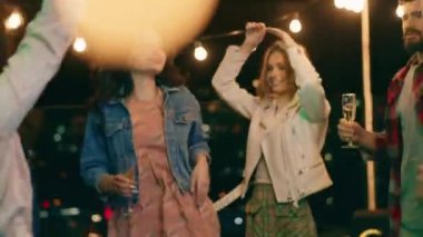 Çok ırklı insanlar terasın tepesinde eğleniyorlar. Gece dansını seviyorlar. Telefonlarıyla fotoğraf ve video çekiyorlar. ARRI Alexa Mini 'de çekilen.