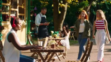 İki güzel kadın parkta kırmızı kablosuz kulaklık takan ve masada oturan arkadaşlarına doğru yürüyorlar.