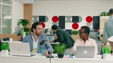 Çok büyük bir ofiste, mavi takım elbiseli çok çekici bir adam gülüyor ve yakışıklı Afrikalı iş arkadaşı arasında konuşuyor.