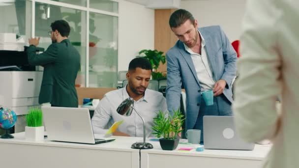 У дуже новому офісі, двоє співробітників мають глибоку інтелектуальну розмову, і їх менеджер з синім костюмом приходить, щоб допомогти їм, поки він залишає чоловіка на задньому плані — стокове відео