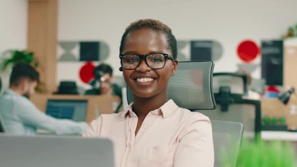 Uma jovem muito linda com cabelo curto e óculos está sorrindo continuamente como a câmera, enquanto ela está em seu escritório. 4K — Vídeo de Stock