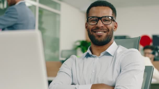 Een brede schouder zwarte man is in zijn fel verlichte kantoor, hij kruist zijn armen en grijnst breed terwijl hij naar de camera kijkt — Stockvideo
