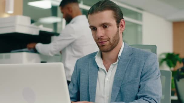 Ein sehr schöner weißer Mann sitzt in seinem Stuhl im Büro, er trägt einen hellblauen Anzug und lächelt, während er seine Arbeit am Laptop verrichtet. ARRI — Stockvideo