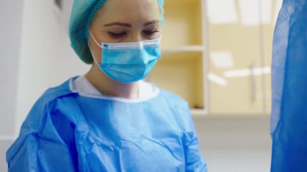 In front of the camera female nurse assistant helping get dressed to the doctor before a surgical operation on the protective equipment — Stock Video