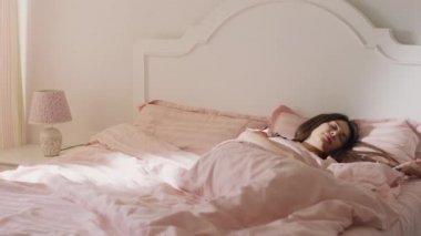 Odasındaki güzel güneş ışınlarıyla uykusundan yükselen uzun kahverengi saçlı bir kadının çekimine kapanış.