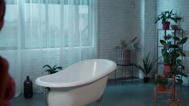 W dużej łazience z uprawianymi roślinami pani chce wziąć kąpiel zdejmuje różową piżamę. Strzał na ARRI Alexa Mini. — Wideo stockowe