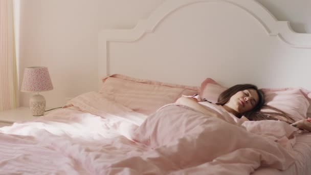 A closing in shot of a woman with long brown hair rising from her slumber with the beautiful sun rays in her room — Stock Video