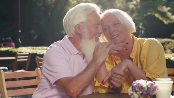 Preciosa pareja de edad mirando muy carismático primer plano de la cámara abrazándose entre sí en el medio del parque en la cafetería — Vídeos de Stock