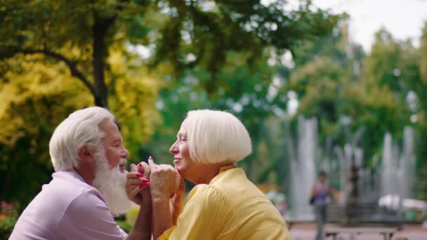Gelukkig oud echtpaar erg romantisch in het midden van het park bij cafe knuffelen handen en kijken elkaar aan en bespreken samen. Neergeschoten op ARRI Alexa Mini. — Stockvideo