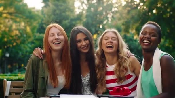 A close up of four friends that are very beautiful sitting at a table outside in the park, laughing and enjoying eachother a company — Stock Video