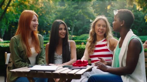 Un bellissimo e molto vicino gruppo di amiche ragazze sono in un parco, seduti a un tavolino con tutte le loro cose su di esso, stanno avendo battute e ridendo insieme, godendo di essere l'uno con l'altro — Video Stock