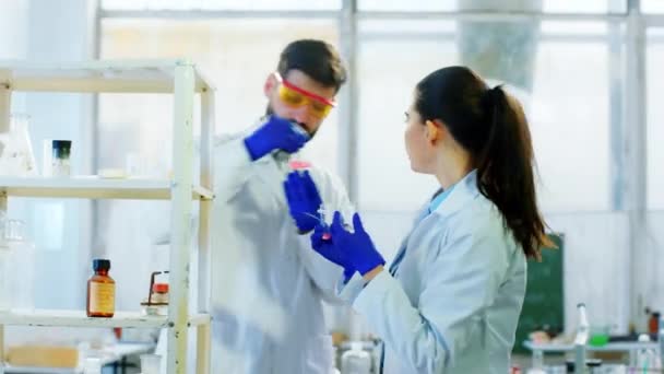 Концепция исследования и биохимии ученый женщина и ее помощник мужчина вместе смешивая некоторые химические жидкости в стеклянных ваннах, чтобы сделать эксперимент — стоковое видео