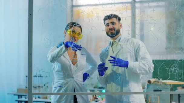 Knappe teamwetenschapper vrouw en man die de chemische formule van het transparante bord in het biotechnologielaboratorium analyseren — Stockvideo