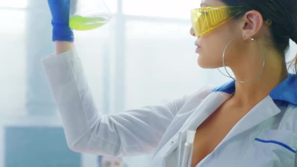 镜头前的细节实验室里漂亮的女药剂师拿着一个装有化学物质的玻璃管让她穿上防护服做出化学反应 — 图库视频影像