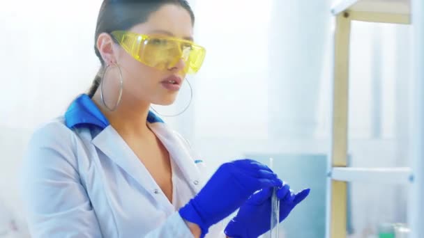 A kémiai laboratóriumban vonzó női tudós dolgozik a projekten, valamilyen kémiai anyagot használva az üvegcsövekbe. — Stock videók