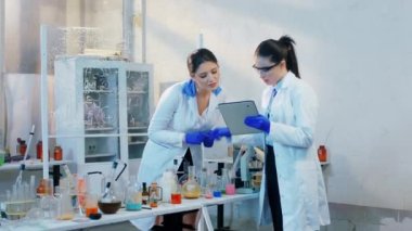 Kimya laboratuvarında karizmatik bir grup genç bilim adamı deneylerin sonuçlarını yazmak için dijital tablet kullanarak bir proje üzerinde çalışıyorlar.