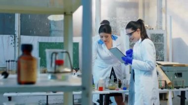 Kimya laboratuarında iki karizmatik kadın ve bir erkek tıp öğrencisi bazı deneyler yapıyor kimyasal formülü karıştırıp dijital tablet kullanıyorlar.