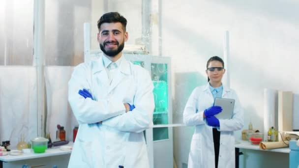 Kimya laboratuvarının ortasında kameranın önünde poz veren mutlu ve heyecanlı kadın ve erkek bilim adamı ilaç laboratuarı ve biyoteknoloji konseptine bakıyorlar. — Stok video