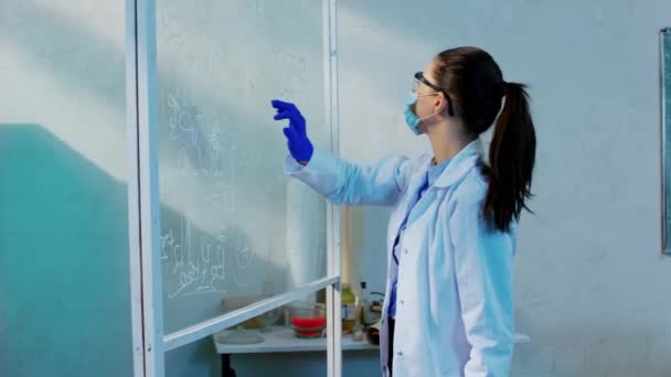 En el laboratorio de química atractiva mujer jóvenes científicos analizando el tablero transparente de una fórmula química muy concentrada que llevaba equipo de protección completa — Vídeos de Stock