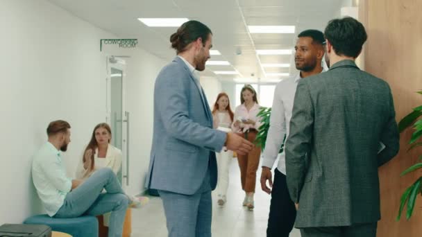 Dos mujeres trabajadoras de aspecto amable están caminando rápidamente por el pasillo de la oficina mientras pasan por tres hombres de negocios de aspecto inteligente en una conversación — Vídeos de Stock