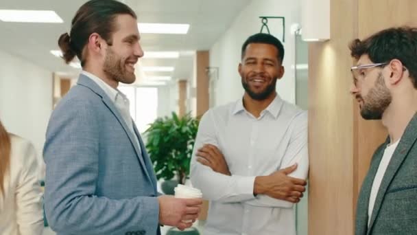 Eine Nahaufnahme von drei Arbeitskollegen, die im Flur lachen und über Arbeitssachen reden — Stockvideo