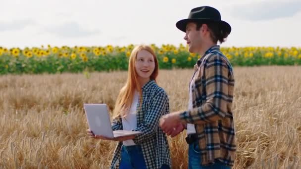 Современная фермерская пара берет ноутбук посреди пшеничного поля и анализирует урожай вместе — стоковое видео