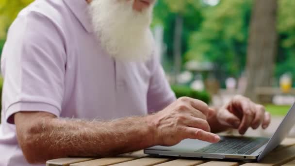 Przystojny staruszek zabiera laptopa do kawiarni i pracuje na świeżym powietrzu pisze coś na laptopie. — Wideo stockowe