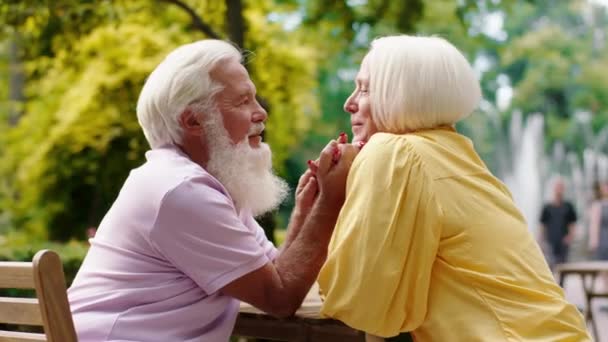 Úžasně vypadající stará žena a muž mají schůzku v kavárně uprostřed parku, drží se za ruce a diskutují s vášní a láskou — Stock video