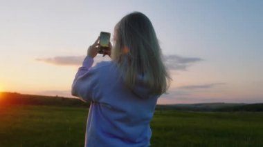 Güzel bir bayan akıllı telefonunu alıp doğada gün batımının muhteşem fotoğraflarını çeker.