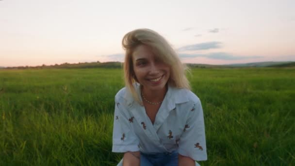 Retrato de primer plano delante de la cámara en la naturaleza en medio de un gran campo verde rubia dama de pelo disfrutar del momento a solas ella mirando a la cámara y sonriendo a lo grande — Vídeo de stock