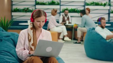 Fasulye torbalı bir odada küçük bir grup insan toplantı düzenlerken bir adam mavi kablosuz kulaklık takıyor ve telefonuna bağlanıyor ve bir kadın müzik dinliyor.