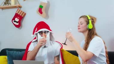 Kameraya yakın. Güzel kadın ve erkeği Noel akşamı kanepede. Noel Baba battaniyesi giyen adama şampanya götür.