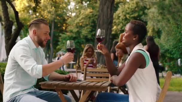 Una asombrosa mujer africana y un hombre blanco están compartiendo vino y cenando juntos en un lugar pintoresco — Vídeos de Stock