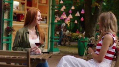 İki güzel kadın parkın dışındaki bir kafede yuvarlak bir masada oturmuş bir konuyu tartışıyor ve bir yudum şarap içiyorlardı.